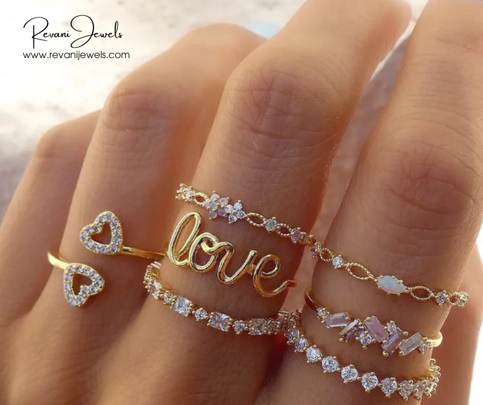 Gold rings with 'love' and heart designs on a hand, branded 'Revani Jewels'.