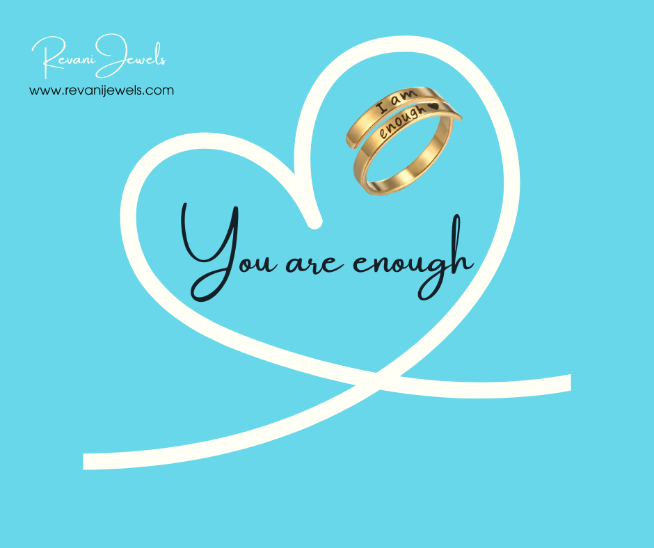 Gold ring on a heart-shaped ribbon with 'You are enough' text on a blue background, featuring Revani Jewels branding.